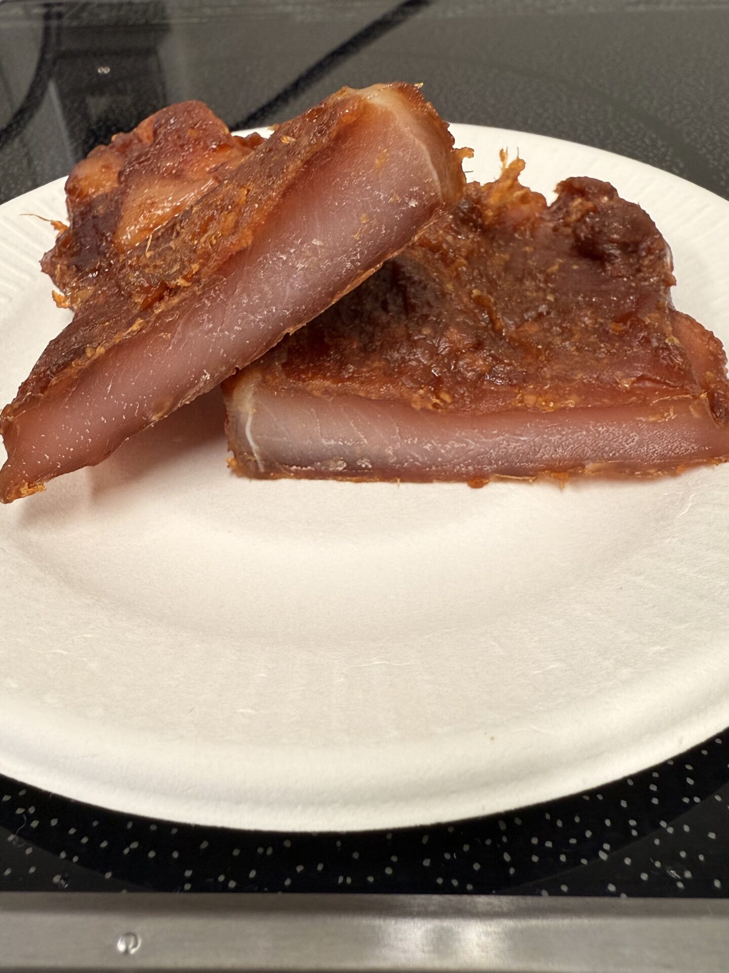 「味噌漬けポークジャーキーの完成品。赤味噌で熟成・乾燥・加熱された豚肉が、光沢のある表面としっとりした食感に仕上がり、白い皿に盛り付けられている。」