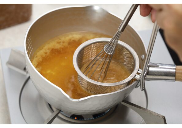 味噌をこし器で溶かしながら鍋に加える調理工程。火を止めた直後の出汁に味噌を丁寧に溶かし入れる、日本の味噌汁の基本的な作り方。