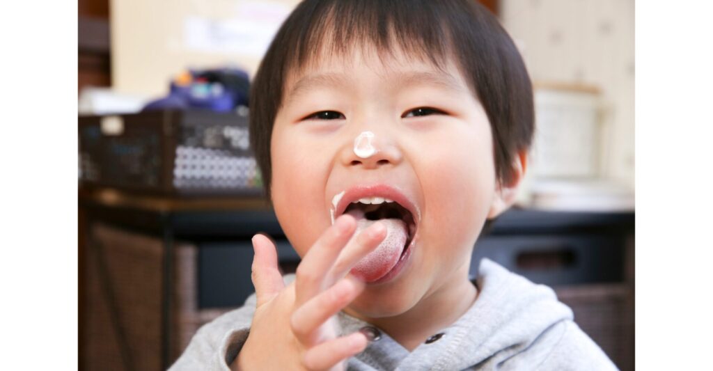 クリームを指につけて味わう幼い子ども。家庭の中で味覚と記憶が育まれる微笑ましい瞬間