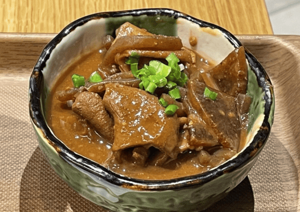 代替テキスト　甘辛い味噌だれで煮込まれた豚肉の味噌煮。青ねぎを添えた陶器の器に盛り付けられ、木製トレイに置かれている