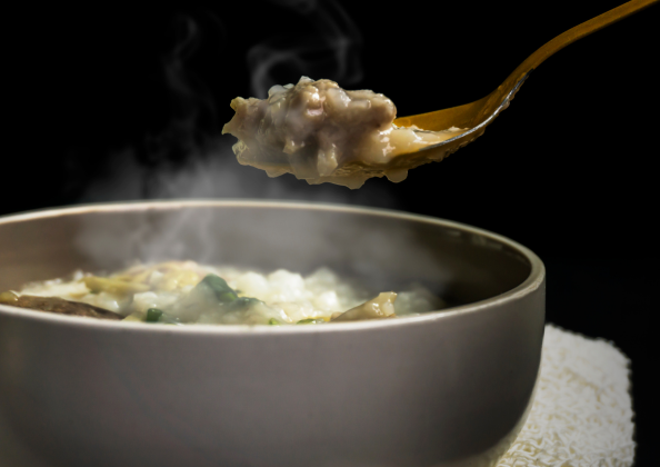 「白い器に盛られた熱々の雑炊から、スプーンですくい上げた一口。肉や野菜の具材が見え、立ちのぼる湯気が旨味と温かさを伝える、冬にぴったりの一品。」